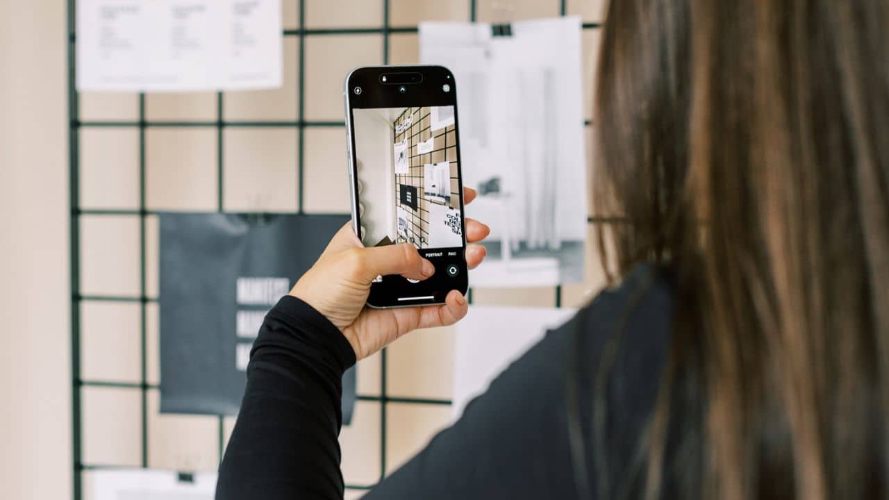 Long-haired person holding up a camera phone to take a photo of a product to create content with,